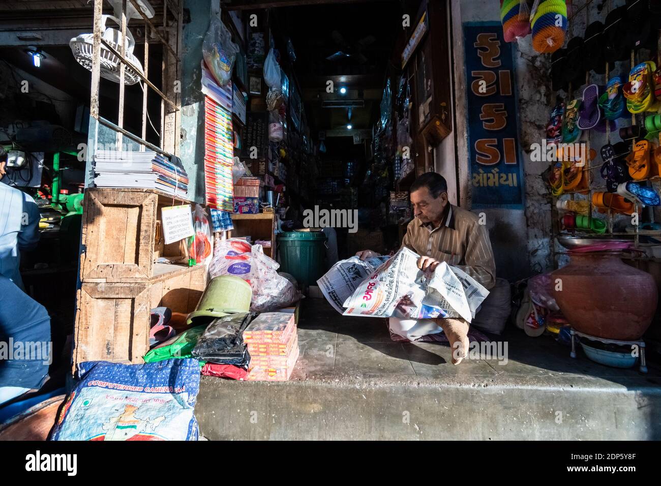 Jamnagar, Gujarat, India - December 2018: An Indian shopkeeper reading a newspaper outside his shop in the market. Stock Photo