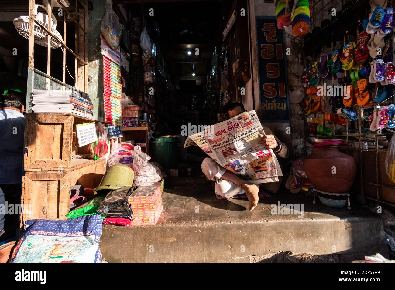 Jamnagar, Gujarat, India - December 2018: An Indian shopkeeper reading a newspaper outside his shop in the market. Stock Photo