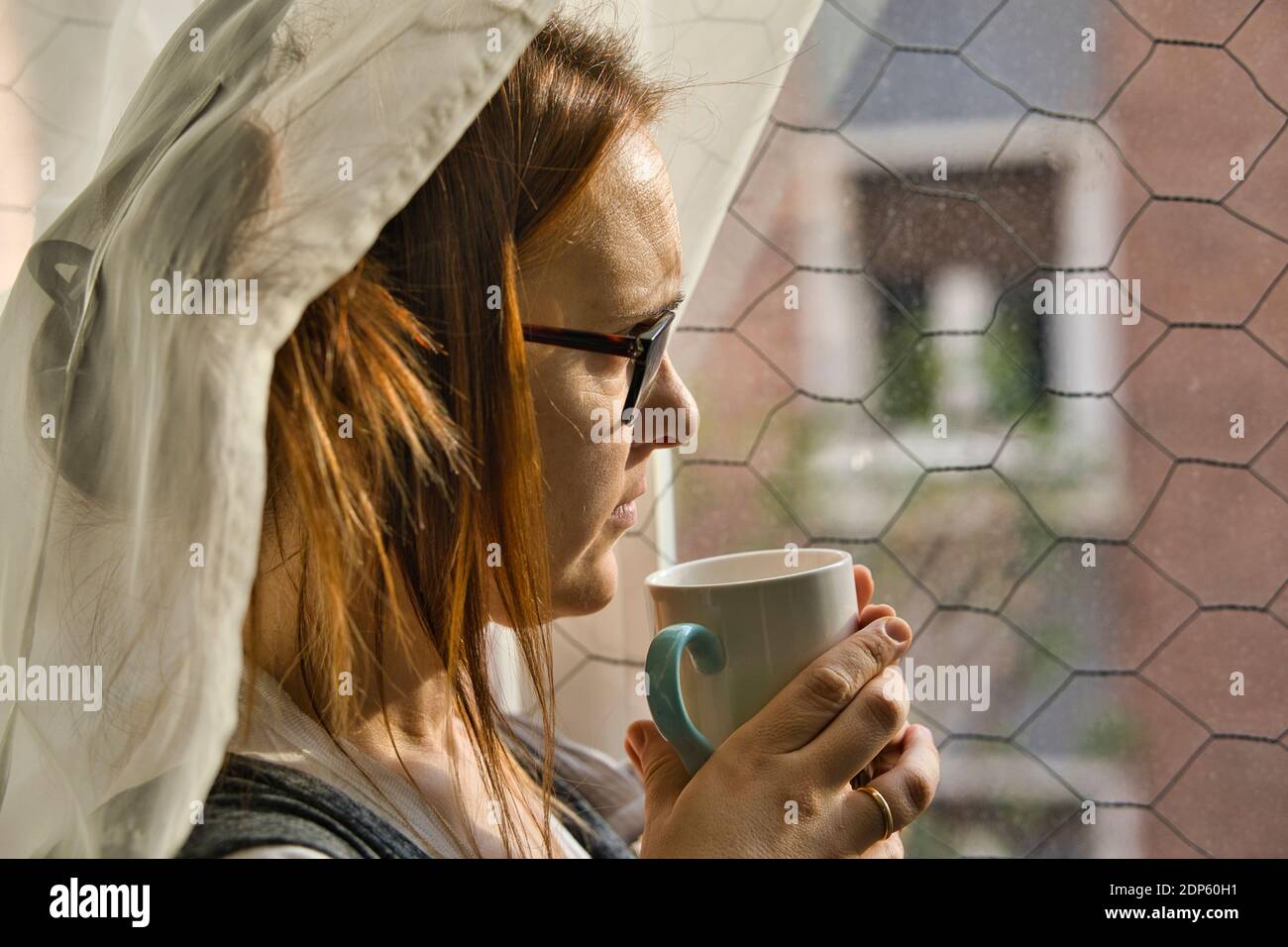beautiful woman looking out the window melancholy on a rainy afternoon having a coffee or tea. bad weather depression concept Stock Photo