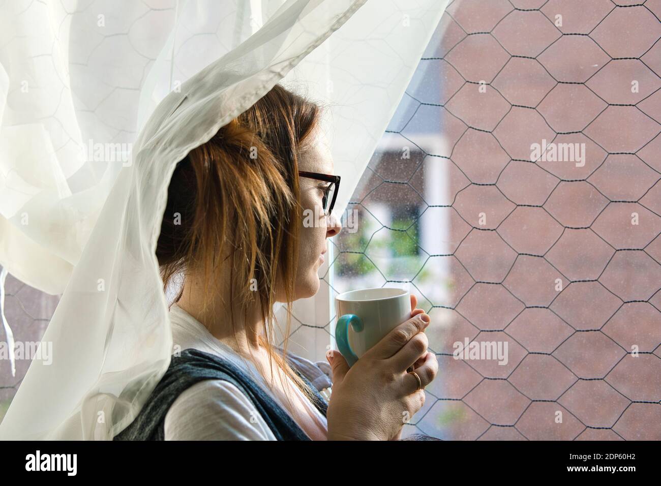 beautiful woman looking out the window melancholy on a rainy afternoon having a coffee or tea. bad weather depression concept Stock Photo