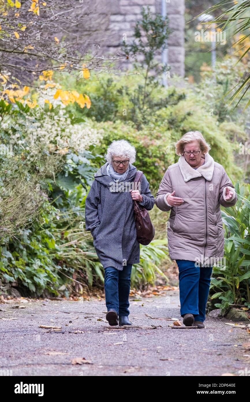 Two mature female friends chatting as they walk through a park. Stock Photo