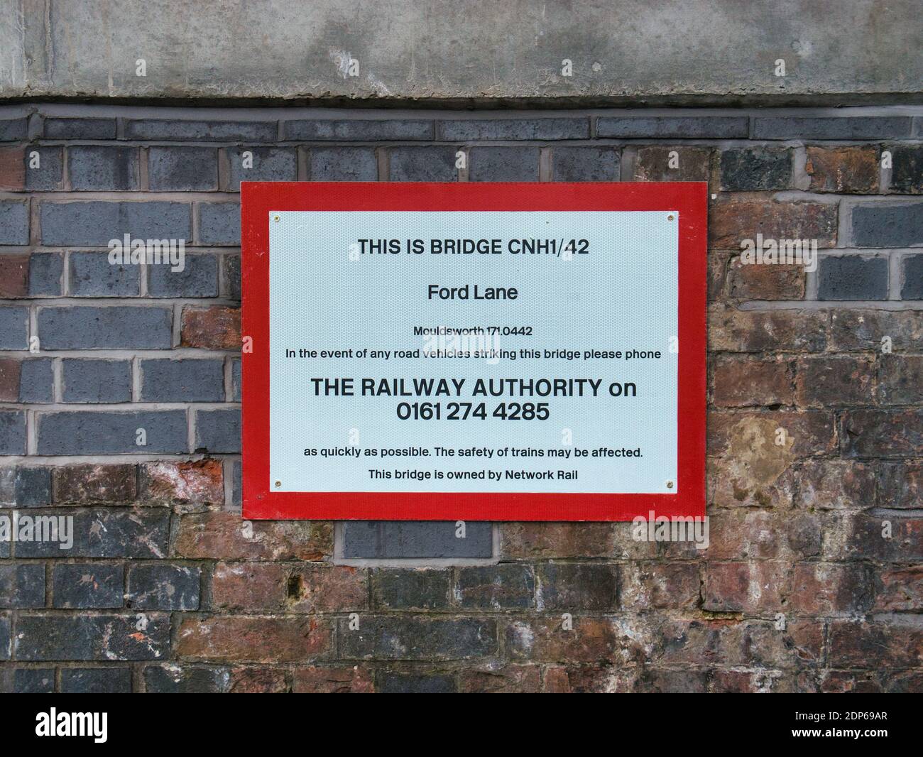 A Network Rail sign under a railway bridge with a phone number to be called in the event of a road vehicle collision with the bridge. Stock Photo