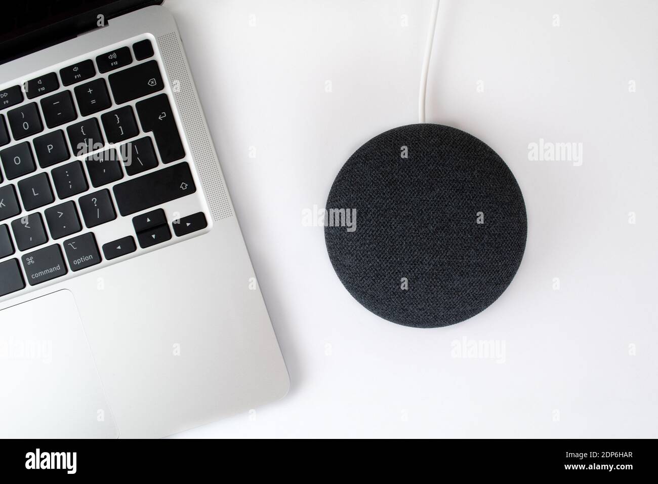London, United Kingdom - 19 December 2020: Charcoal Google Nest Home Mini smart speaker with built in Google Assistant next to a laptop computer. Stock Photo