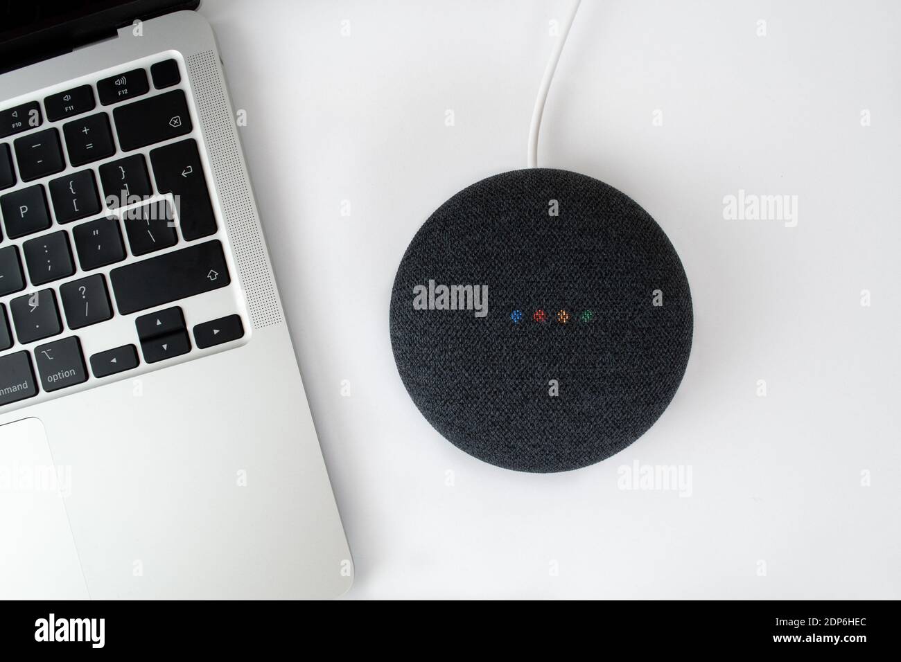 London, United Kingdom - 19 December 2020: Charcoal Google Nest Home Mini smart speaker with built in Google Assistant next to a laptop computer. Stock Photo