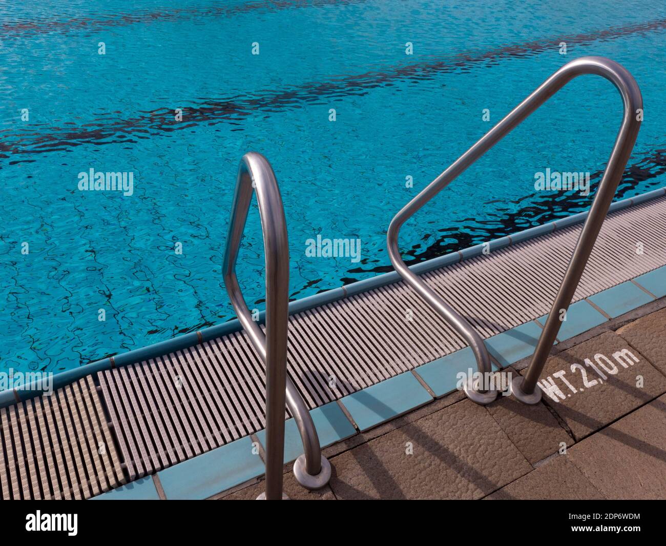 Entrance with a ladder or stairs in the water of a swimming pool. The handles and the railing is made of stainless steel. Stock Photo