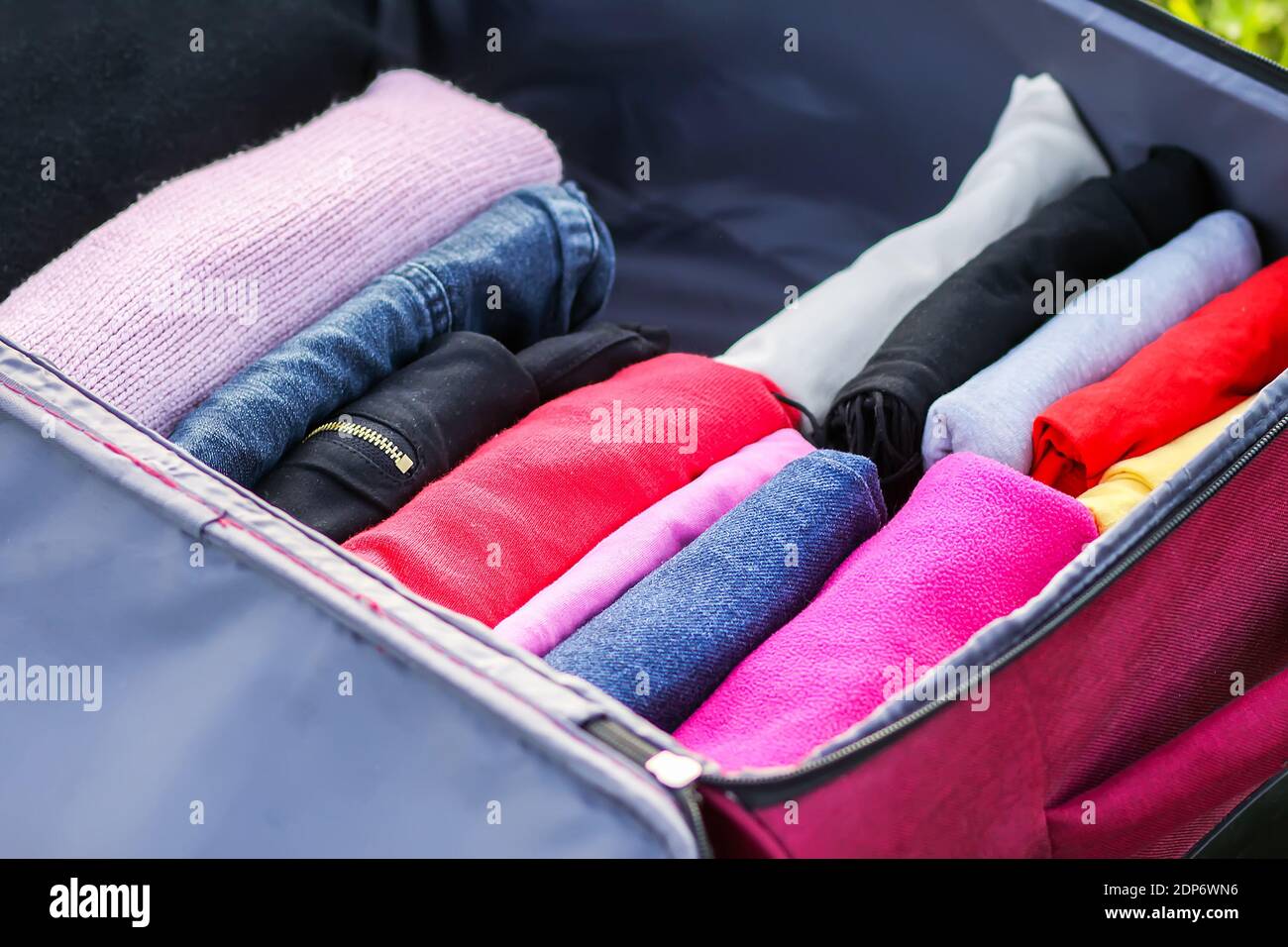 Open suitcase on the green grass with different clothes folded