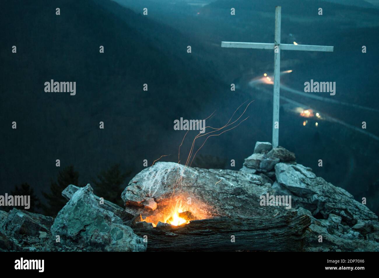 Small fire next to a cross on an exsposed mountain summit Stock Photo
