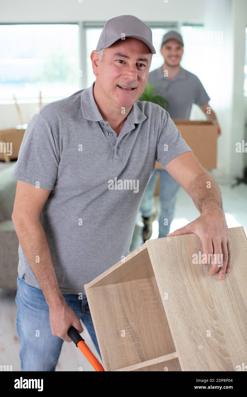 cheerful removals men moving a cupboard on a trolley Stock Photo