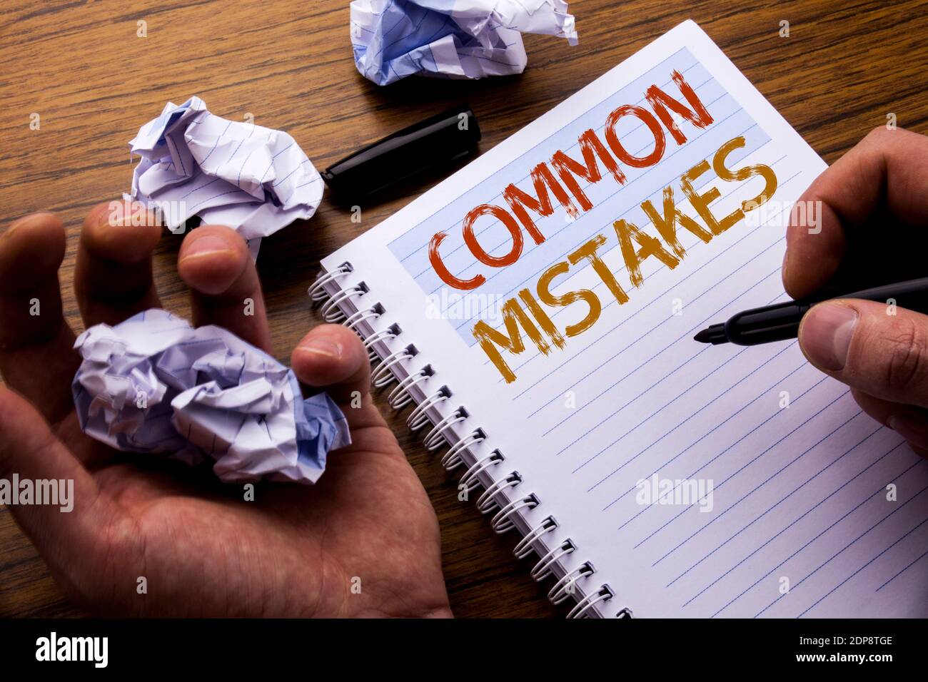 Cropped Hands With Common Mistakes Text On Spiral Notebook At Table Stock Photo