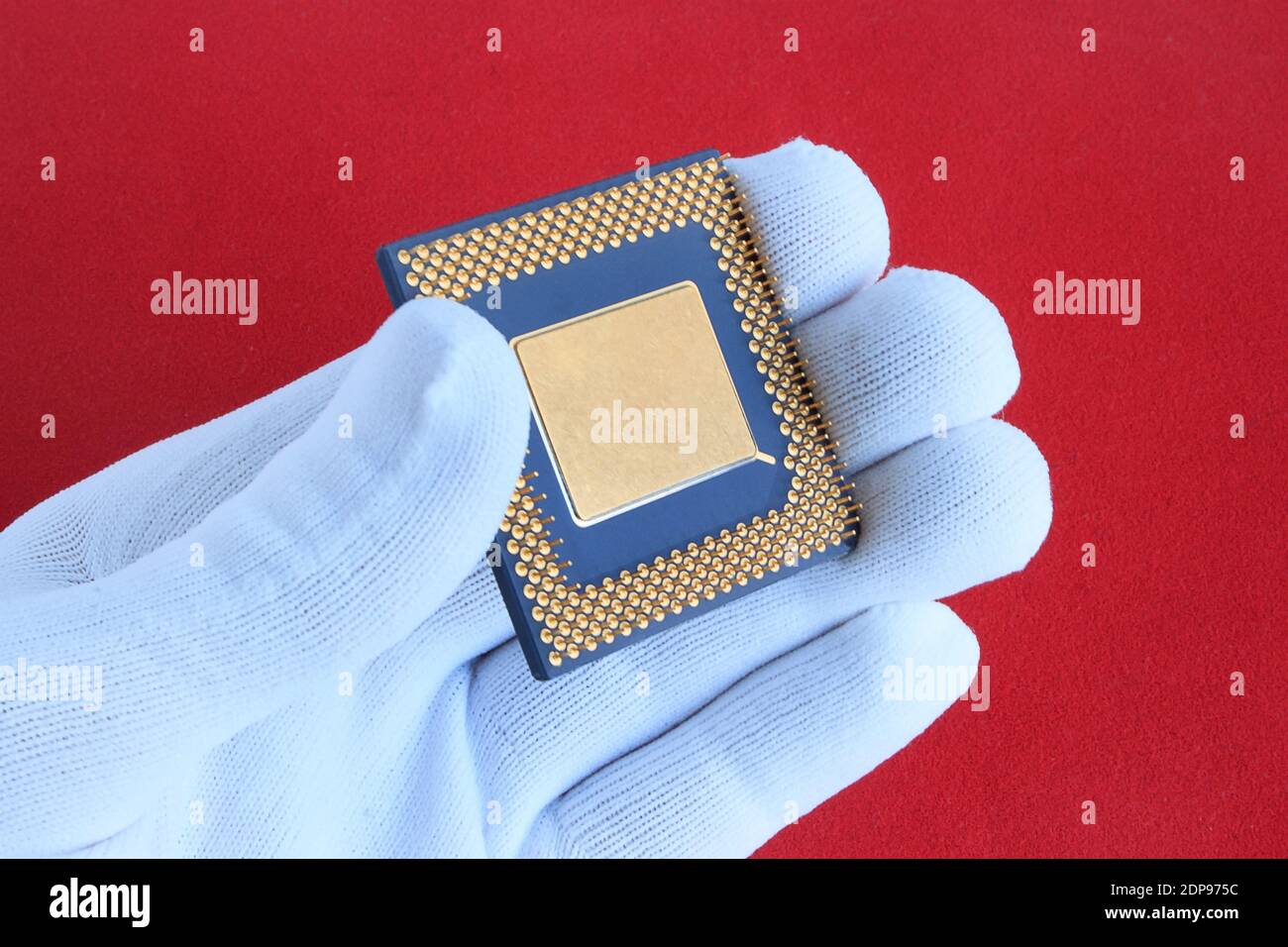 Hand in white glove holds a computer chip. Closeup. Isolated on a red background. Stock Photo