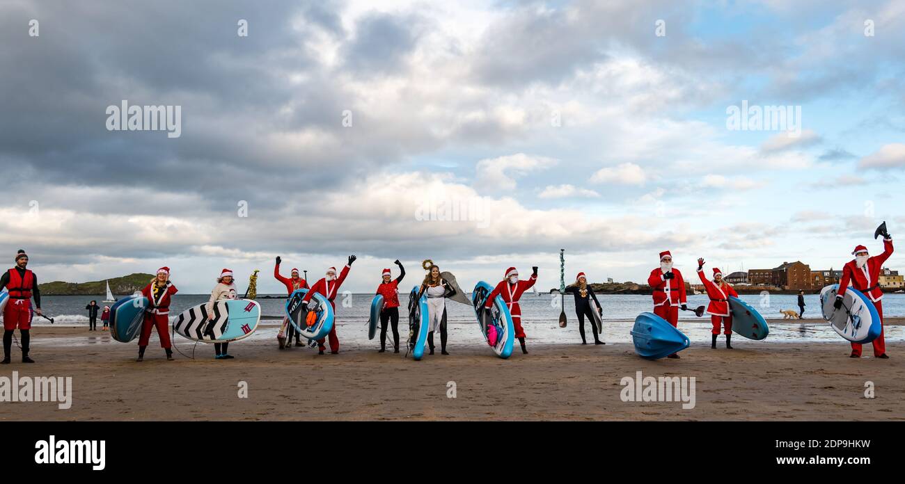 North Berwick, East Lothian, Scotland, United Kingdom, 19th December 2020. Paddle Boarding Santas for charity: a local community initiative by North Berwick News and Views called 'Christmas Cheer' raises over £5,000 funds for families in need. The paddle boarders dressed in Santa costumes pose for a photo on the beach Stock Photo