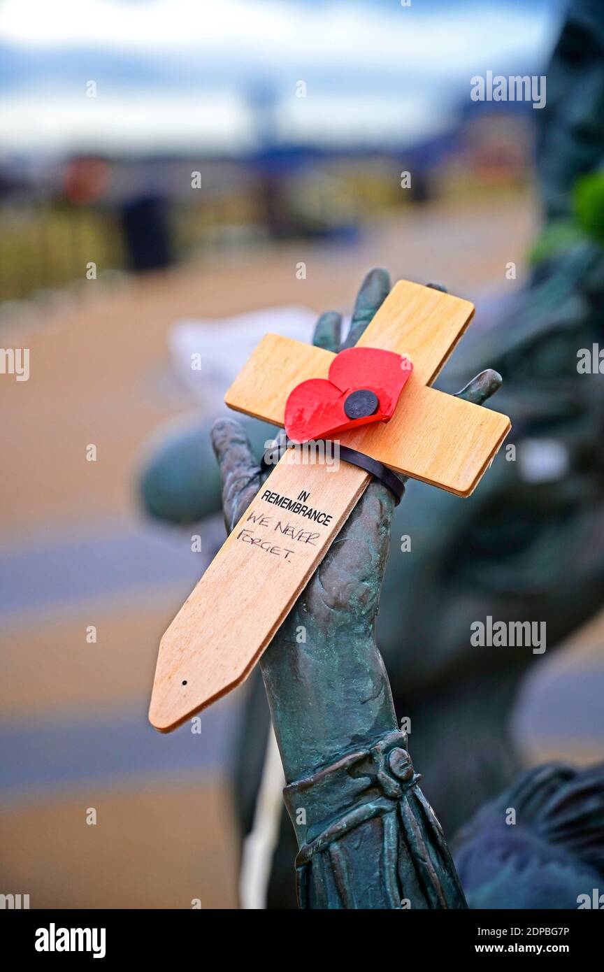 Wooden cross with poppy attached sat in hand of sculpture home
