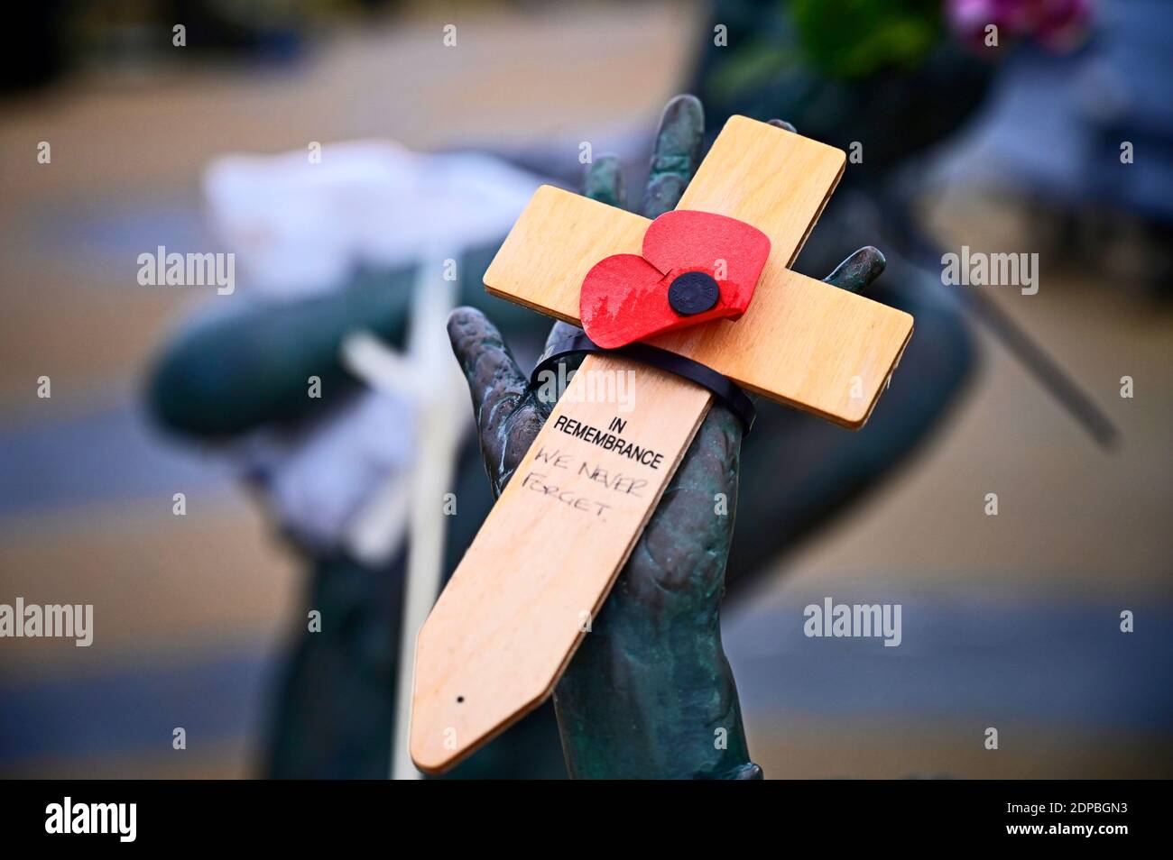 Wooden cross with poppy attached sat in hand of sculpture home