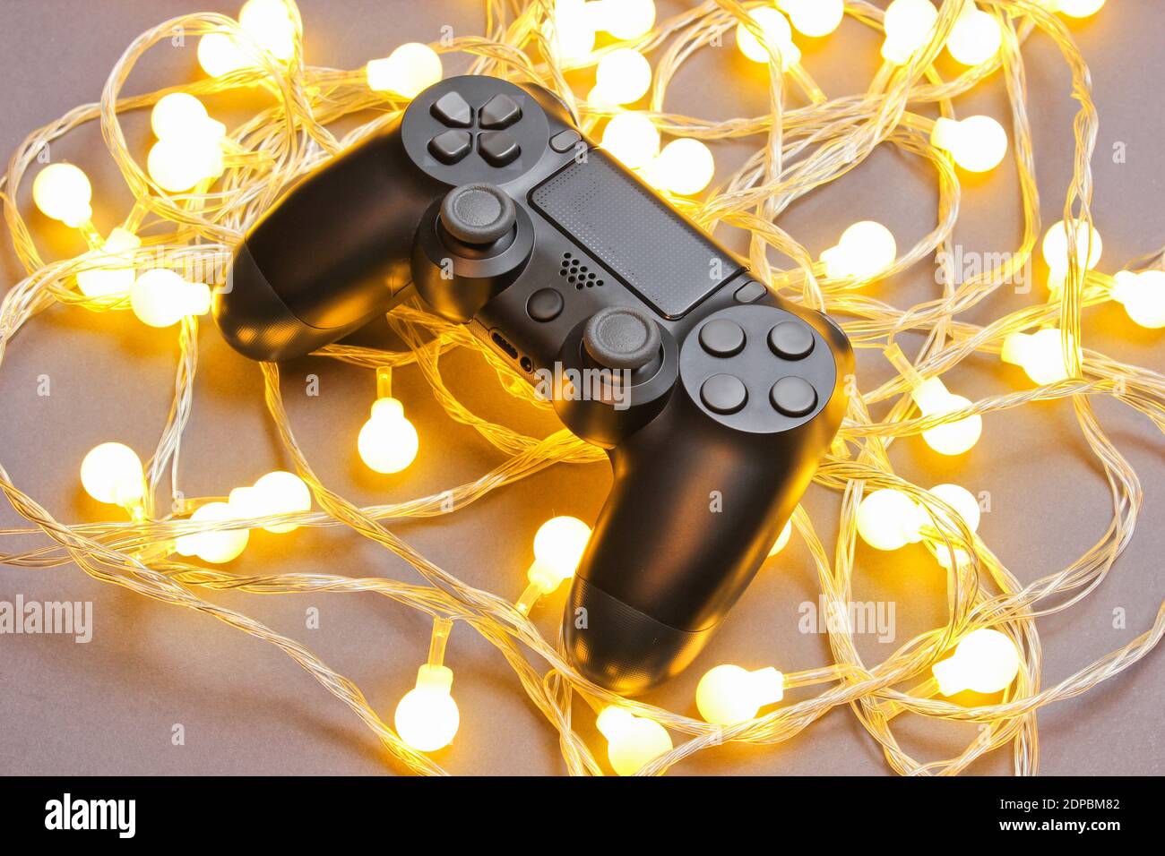 Black plastic gamepad among glowing bright garlands on gray background. Minimalism Stock Photo