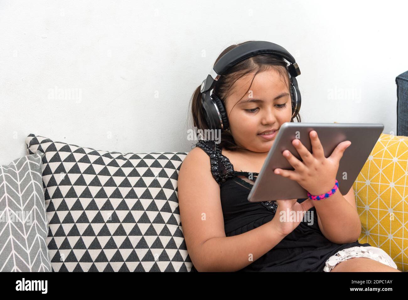 Girl Listening To Music While Using Digital Tablet On Sofa At Home Stock Photo