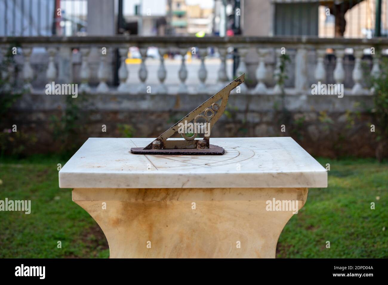 Metal old sundial at Athens National Garden, destination Greece. Antique astronomical sun clock with rusty steel gnomon dial on marble at botanical ga Stock Photo