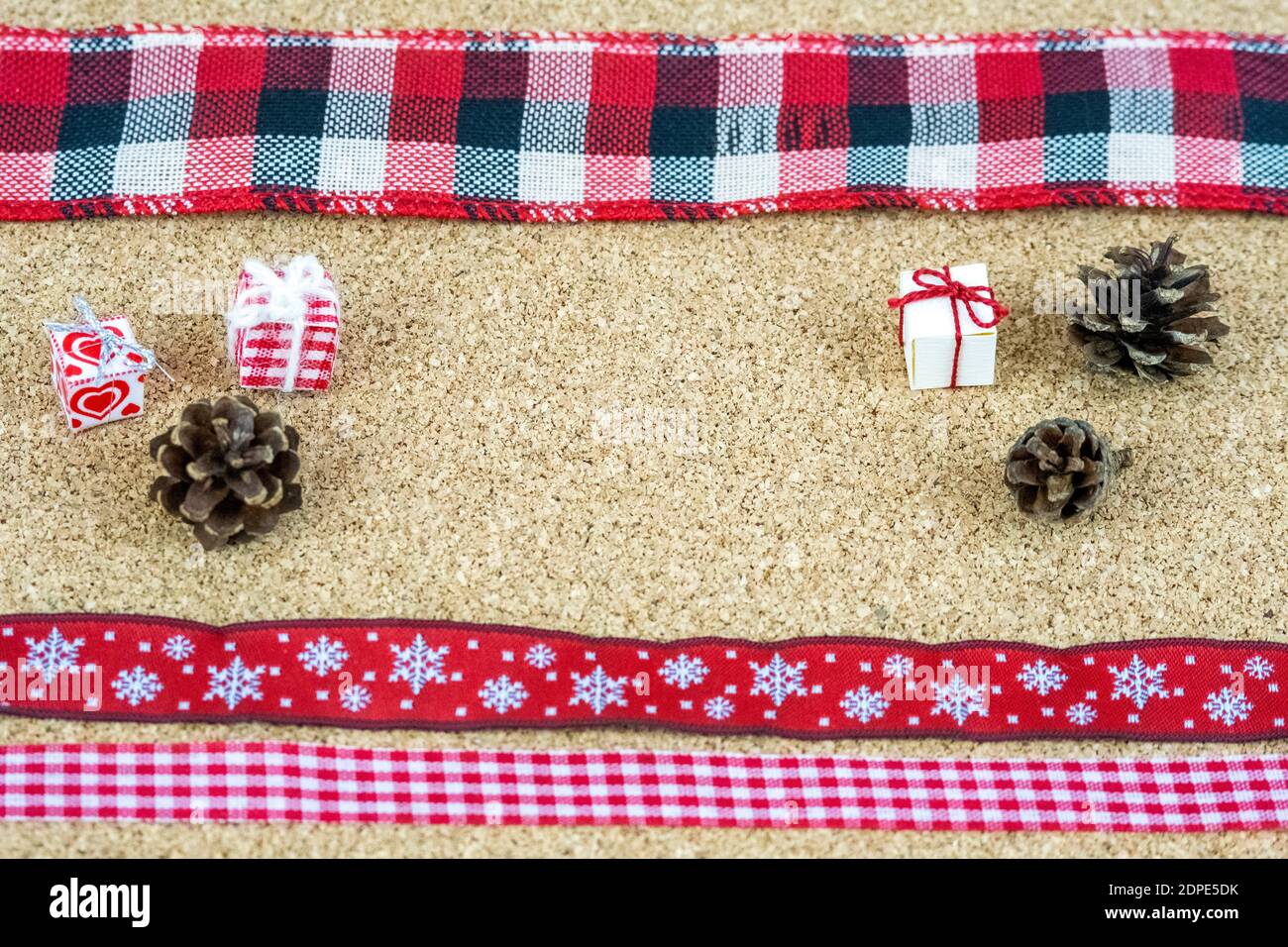 Christmas decoration elements organized on corkwood sheet. Tiny paper boxes, ribbons and small pine cones. Stock Photo