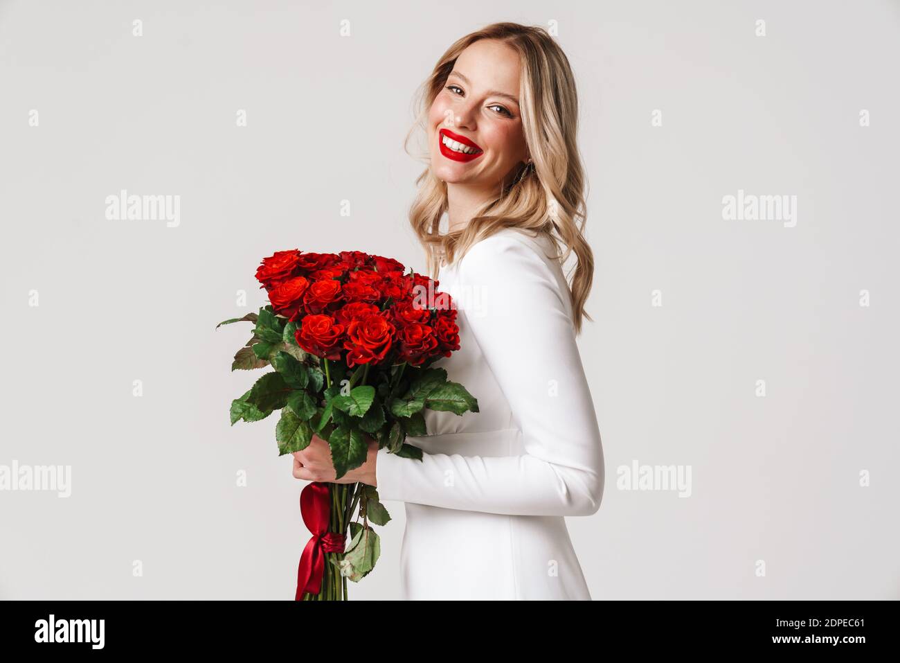 Photo of a young happy woman in white dress holding red roses isolated ...