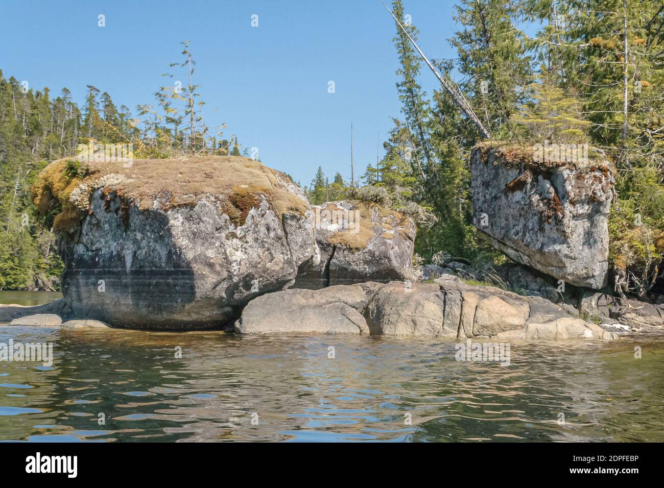 Three huge, moss-topped, textured granite boulders stand close together on a rocky shoreline in a remote wilderness area of coastal British Columbia. Stock Photo