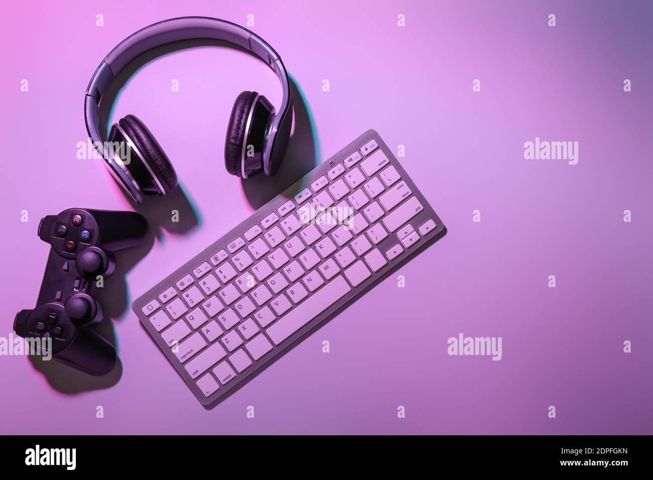 Computer keyboard, gamepad and headphones on color background Stock Photo