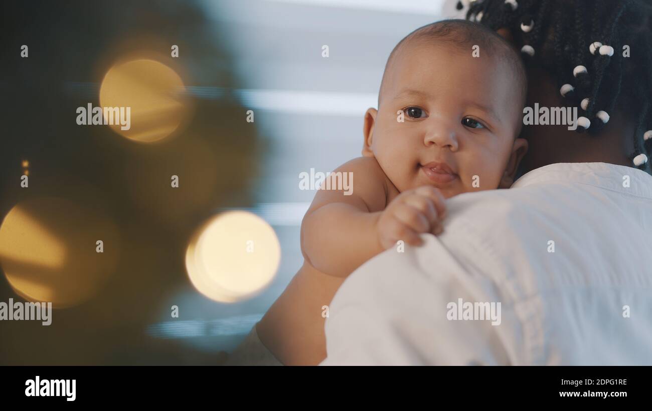 Beautiful newborn mulatto baby enjoying hugs from his black father near christmas tree. Holidays in multiracial family. High quality photo Stock Photo