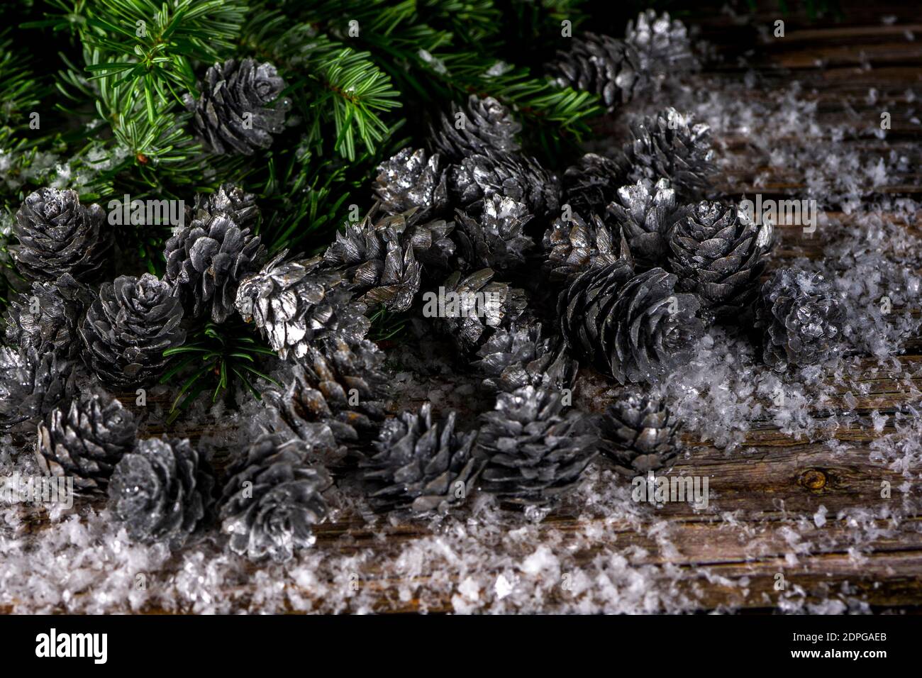 Fir tree branches and silver painted pine cones on a wooden snow ...