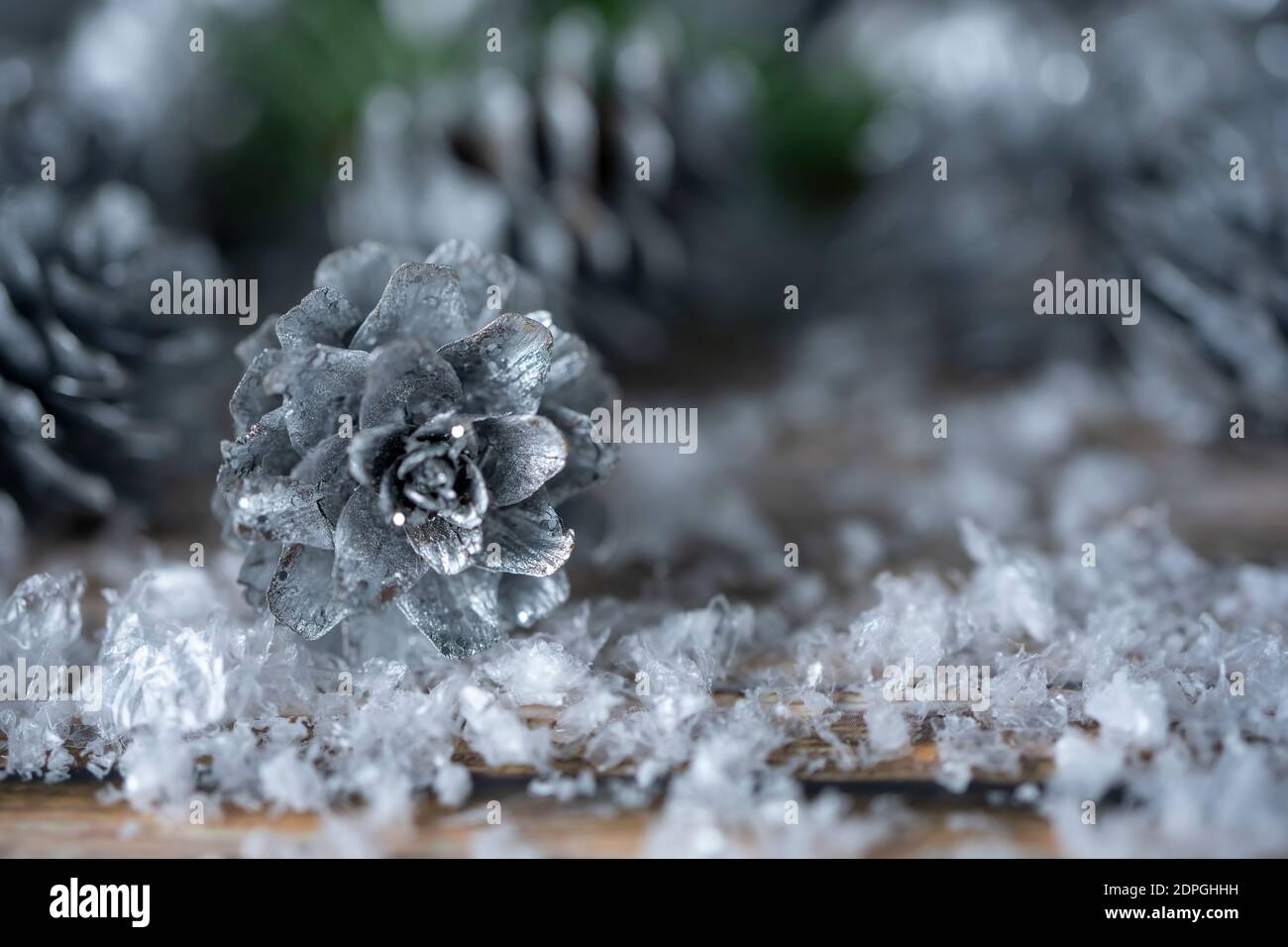 Fir tree branches and silver painted pine cones on a wooden snow ...