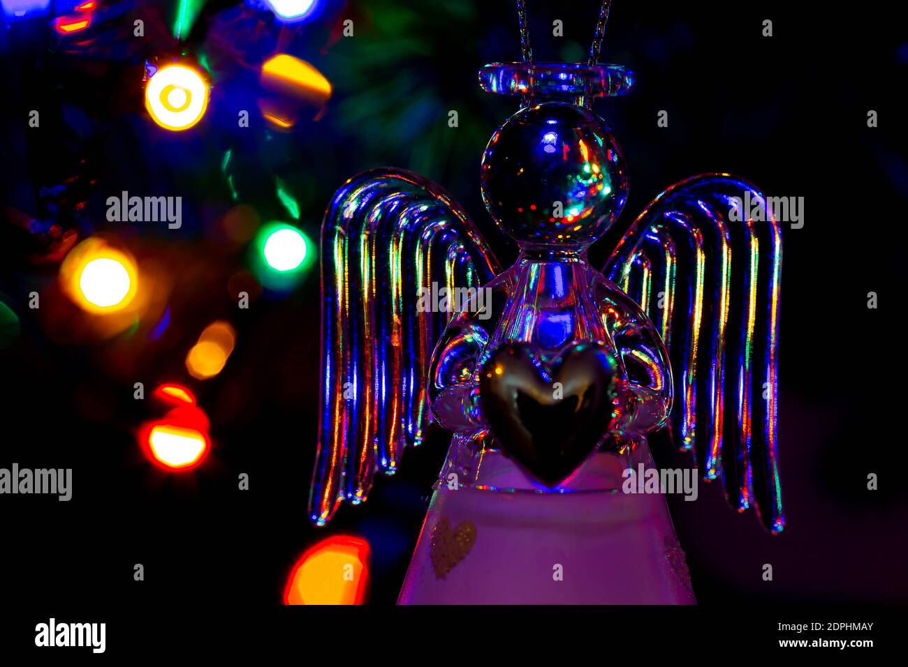 Glass angel holding a heart and supporting a halo with fairy lights on the Christmas tree behind showing as bokeh Stock Photo