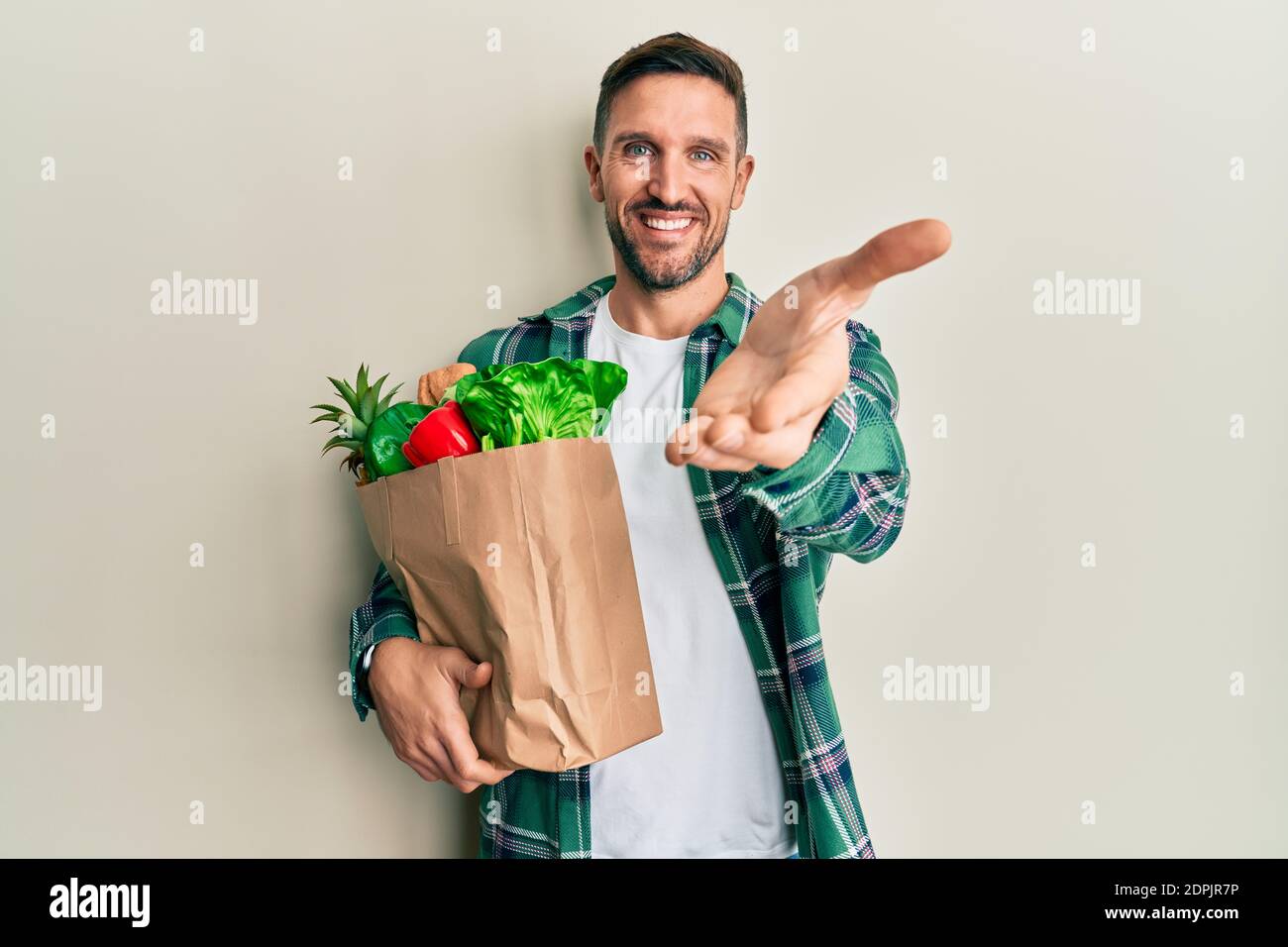 Handsome man with beard holding paper bag with groceries smiling