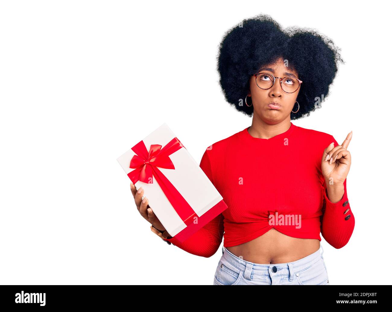 Young african american girl holding gift pointing up looking sad and upset, indicating direction with fingers, unhappy and depressed. Stock Photo