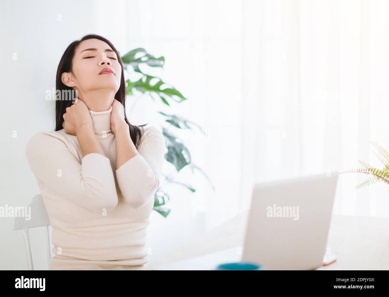 young woman  with neck pain and massaging  neck while working in  office at home Stock Photo