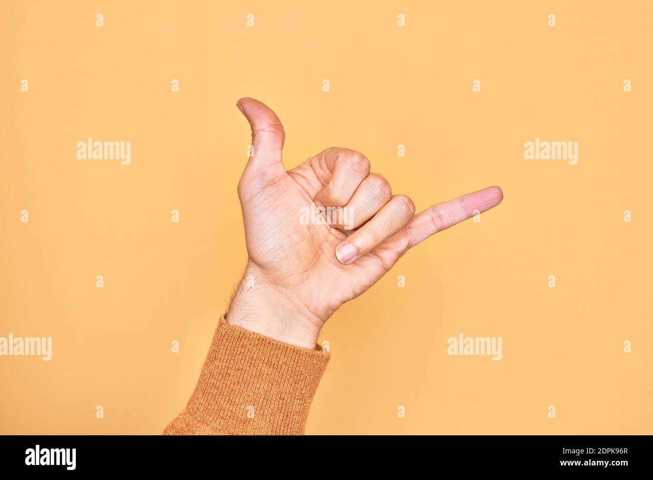 Hand of caucasian young man showing fingers over isolated yellow background gesturing Hawaiian shaka greeting gesture, telephone and communication sym Stock Photo