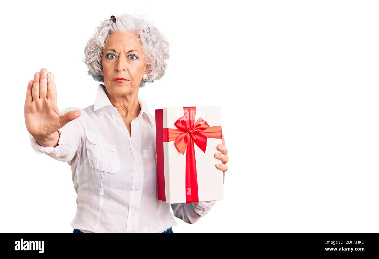 Senior grey-haired woman holding gift with open hand doing stop sign with serious and confident expression, defense gesture Stock Photo