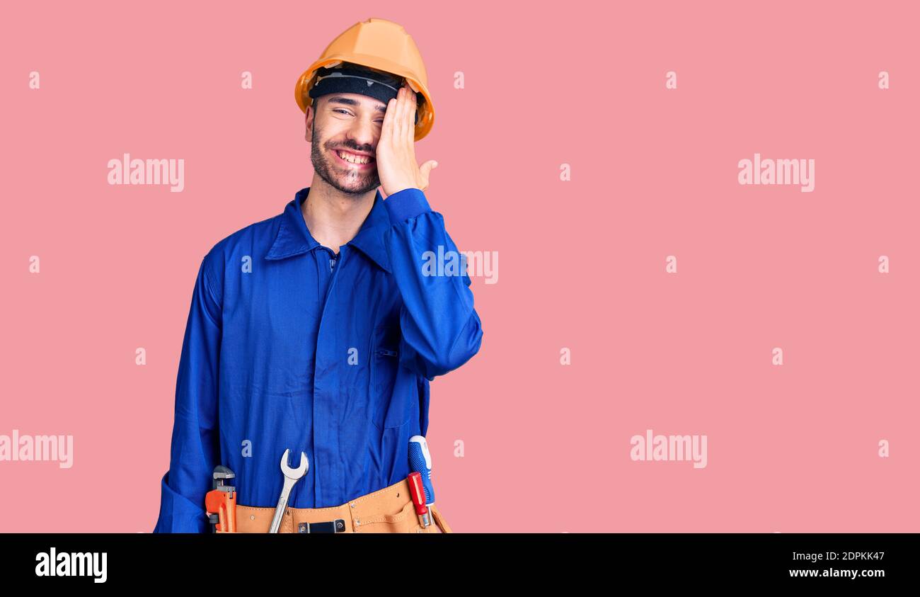 Young hispanic man wearing worker uniform covering one eye with hand ...