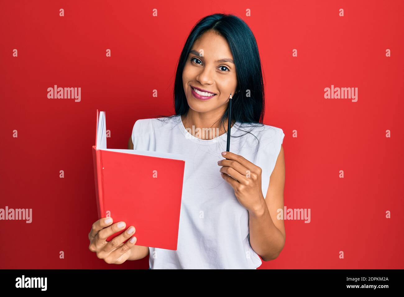 Young african american woman holding book and pencil smiling with a ...