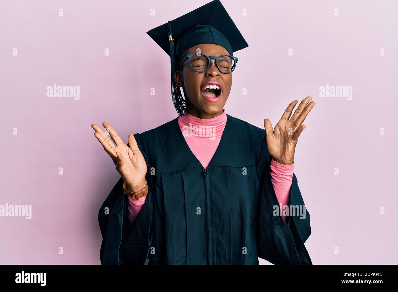 Young african american girl wearing graduation cap and ceremony robe celebrating mad and crazy for success with arms raised and closed eyes screaming Stock Photo