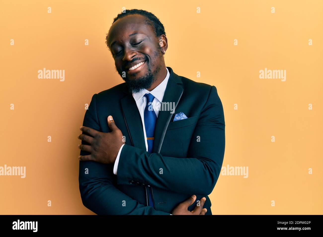 Handsome young black man wearing business suit and tie hugging oneself ...