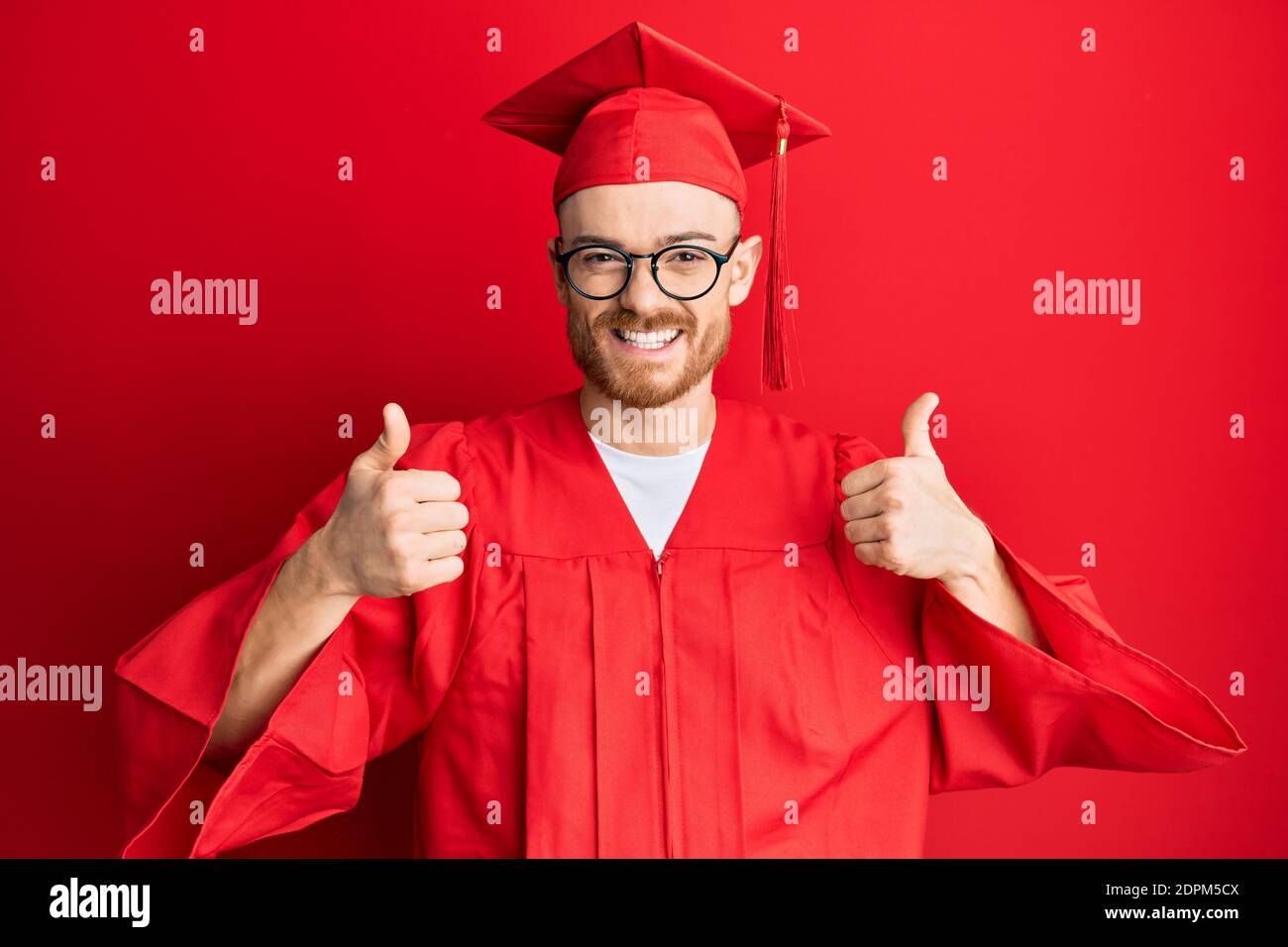 Young redhead man wearing red graduation cap and ceremony robe success ...