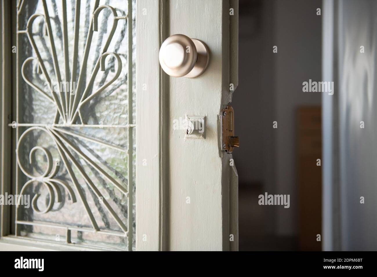 Closeup of old home white wooden door with stained glass and metal lattice. Open vintage entrance doorway with round handle and broken house lock Stock Photo
