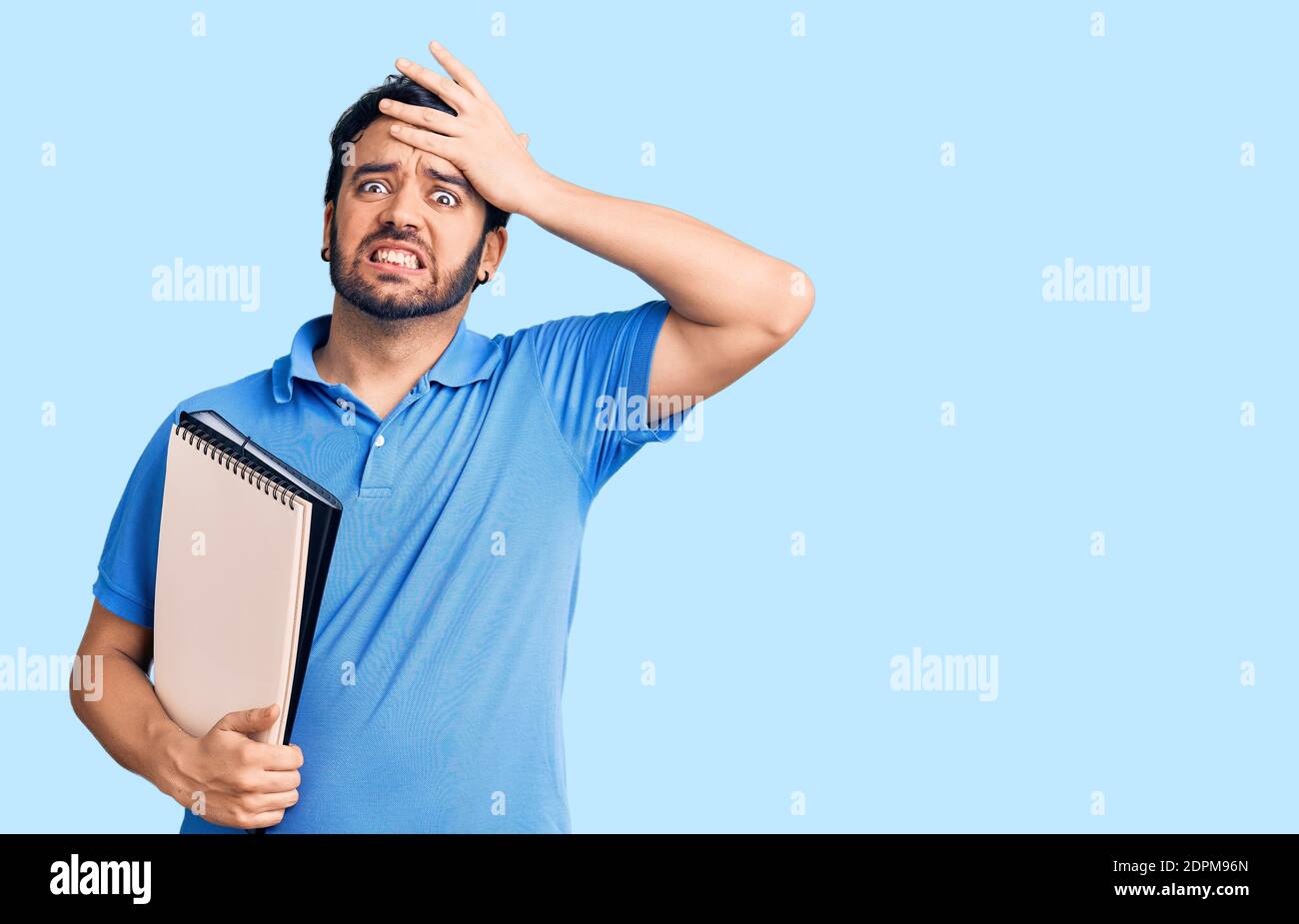 Young hispanic man holding notebook stressed and frustrated with hand ...