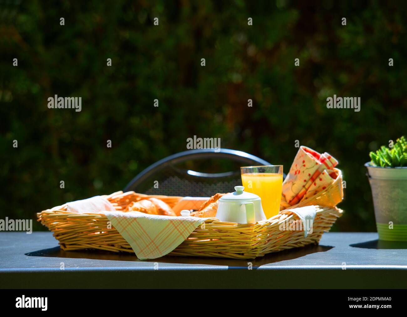 Front view of fresh morning breakfast in wicker plate on open air cafe table top with green bokeh copy space background Stock Photo