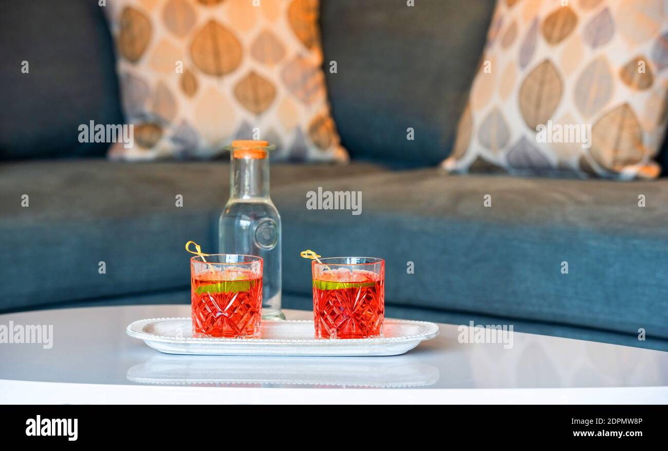Closeup of two campari glasses on white table top surface in lounge interior blur background with grey sofa and autumn pillows Stock Photo