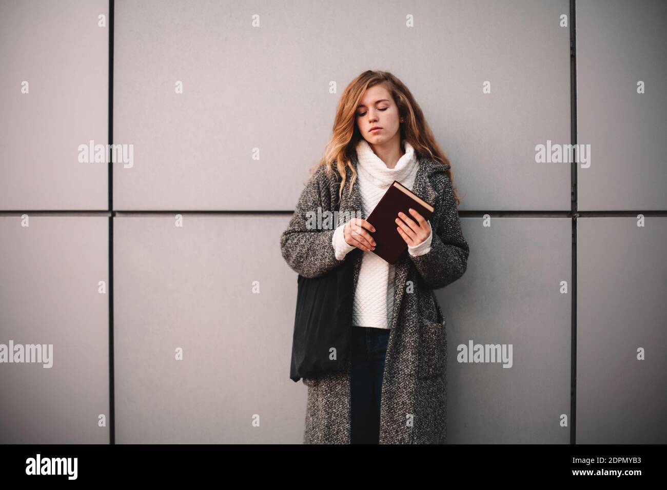 Portrait of thoughtful female student holding book standing against ...