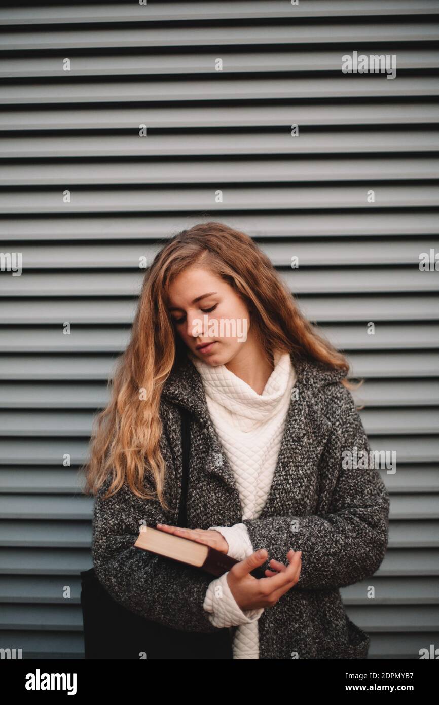 Portrait of teenage student girl holding book standing against gray ...