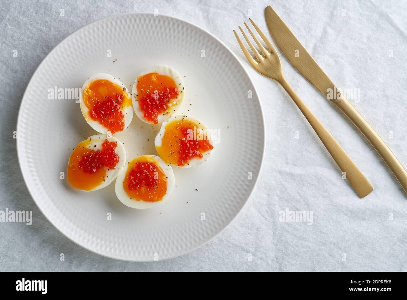 Soft-boiled eggs, peeled and cut into two halves, and salmon caviar lying on white plate. Stock Photo