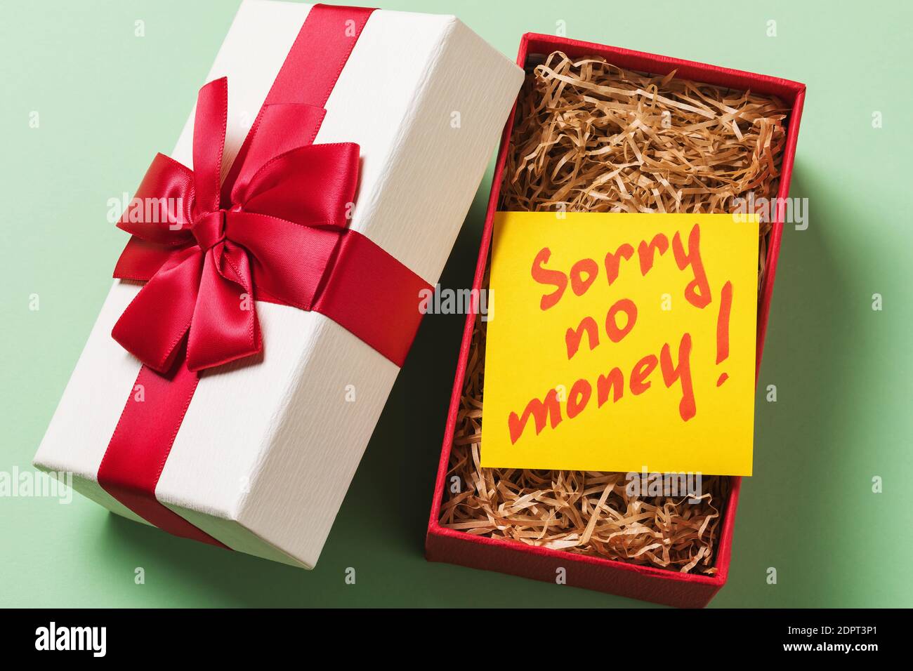 Open gift box with a note inside on a green background. Concept on the topic of lack of money for gifts. Stock Photo