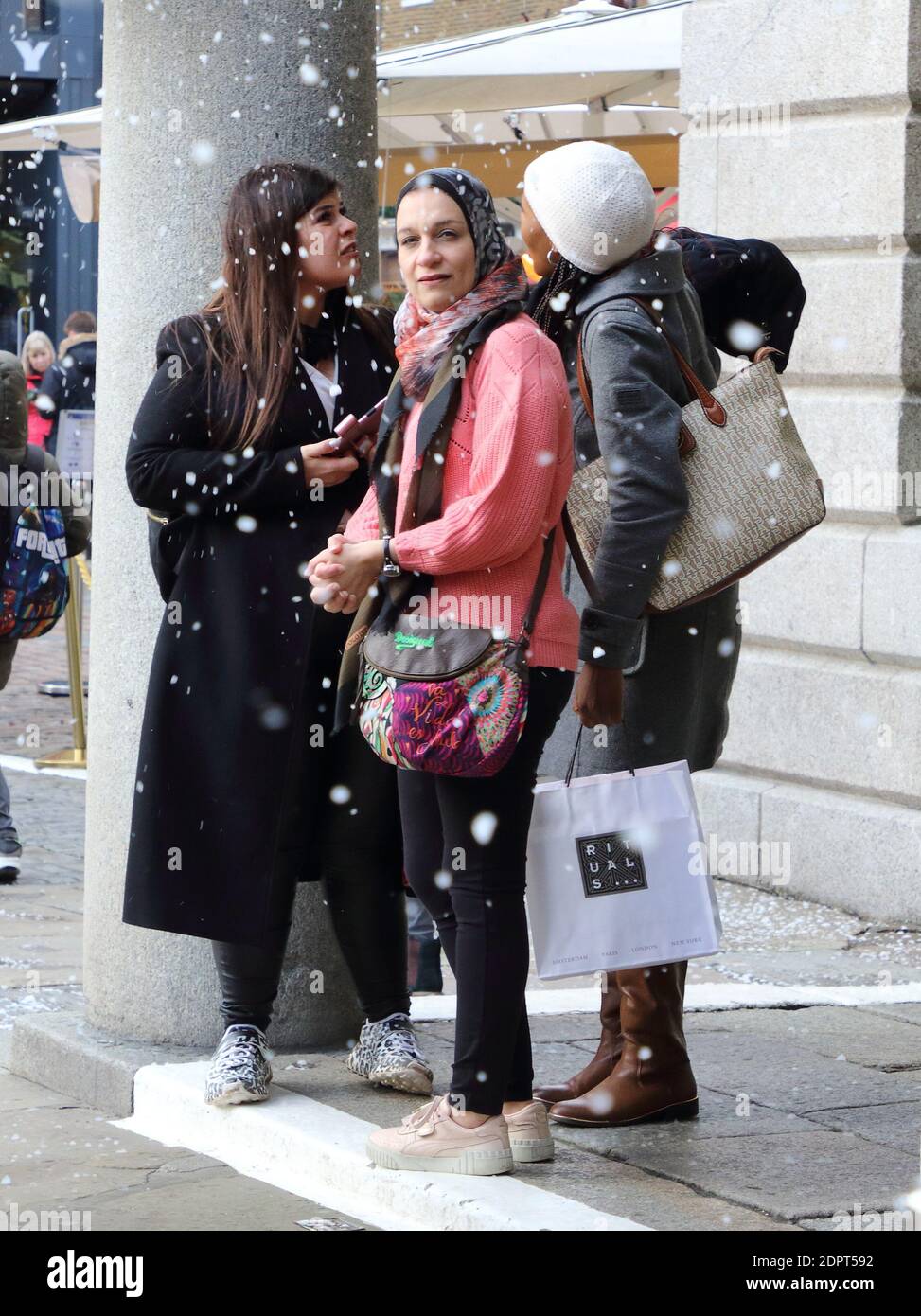 Three women stand together as the fake snowfallsPeople enjoy the