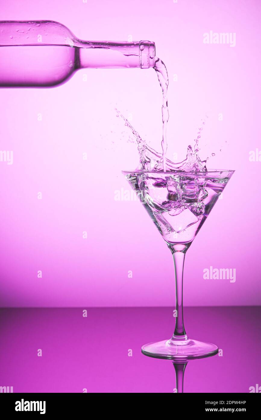 Pink bottle spilling liquid into a cocktail glass and making splash
