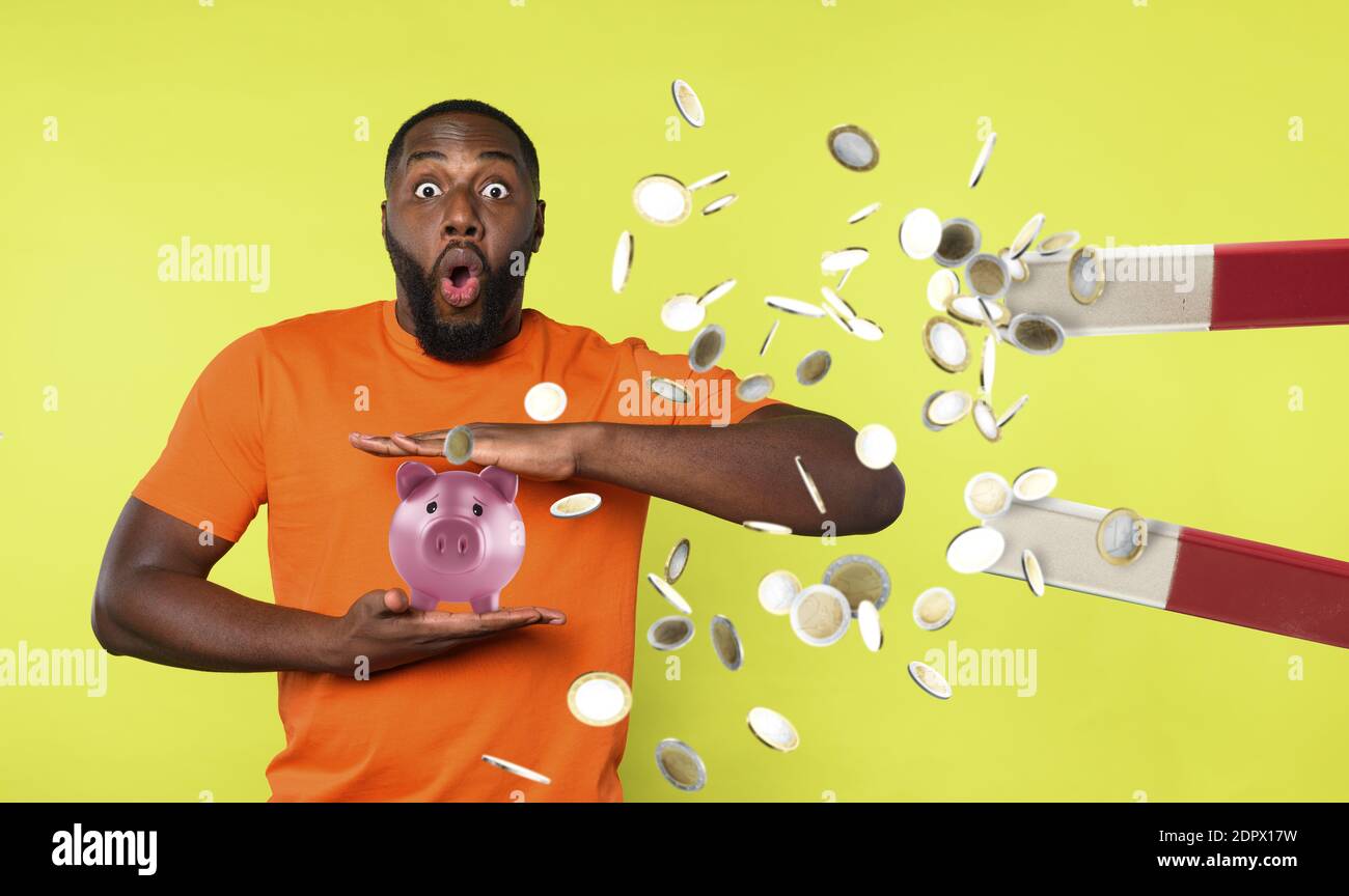 Man tries to protect his piggybank from a big magnet that ruba steals money. concept of money fraud and theft. Green background Stock Photo