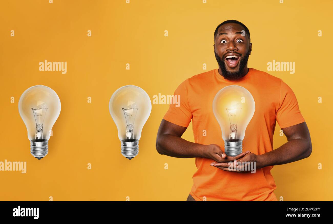 Happy afro man holds a lightbulb with hands. Concept of idea and creativity. Orange background Stock Photo